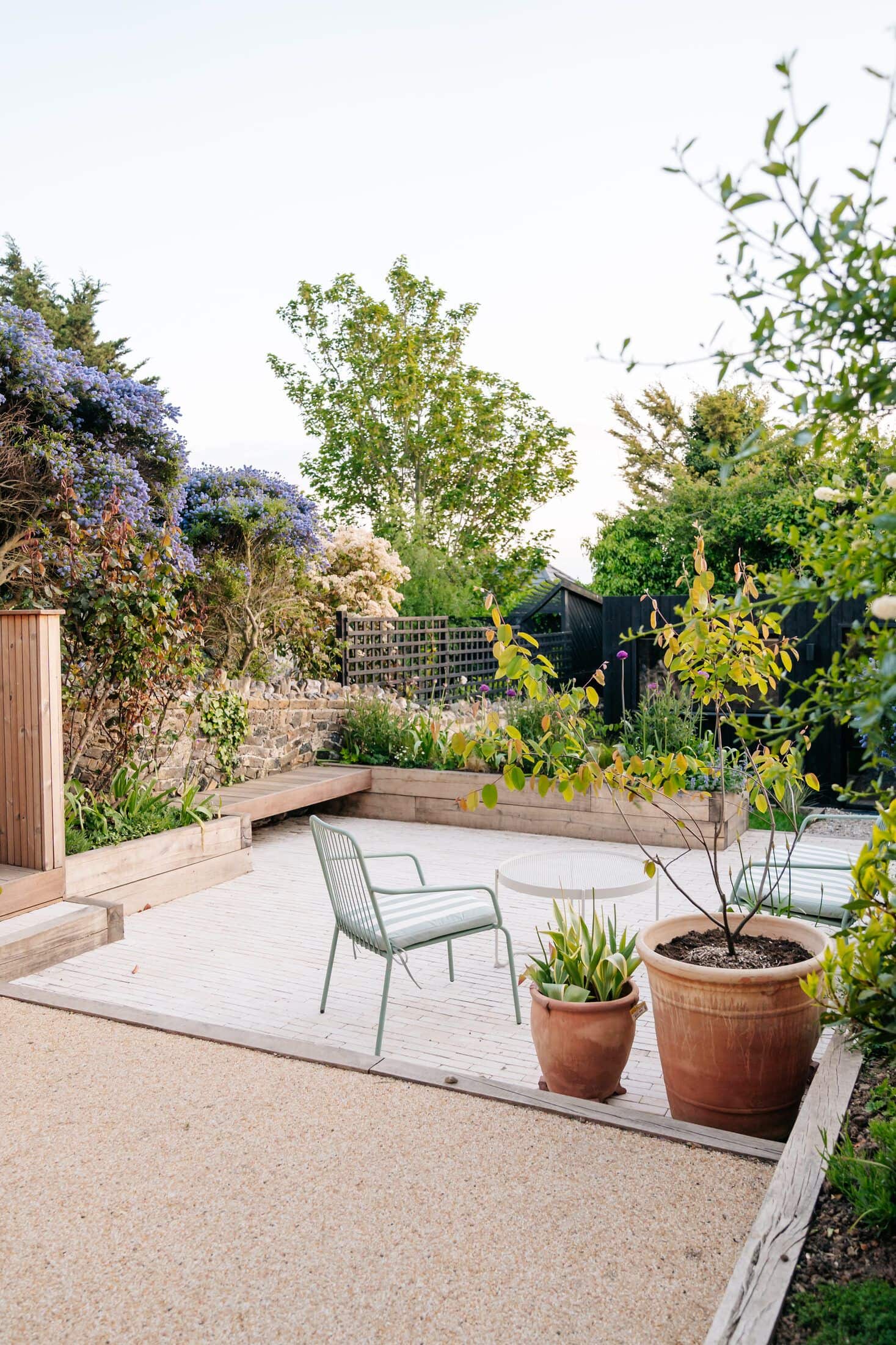 Resin-bound gravel patio with a sage-green chair, terracotta pots and a potted acer