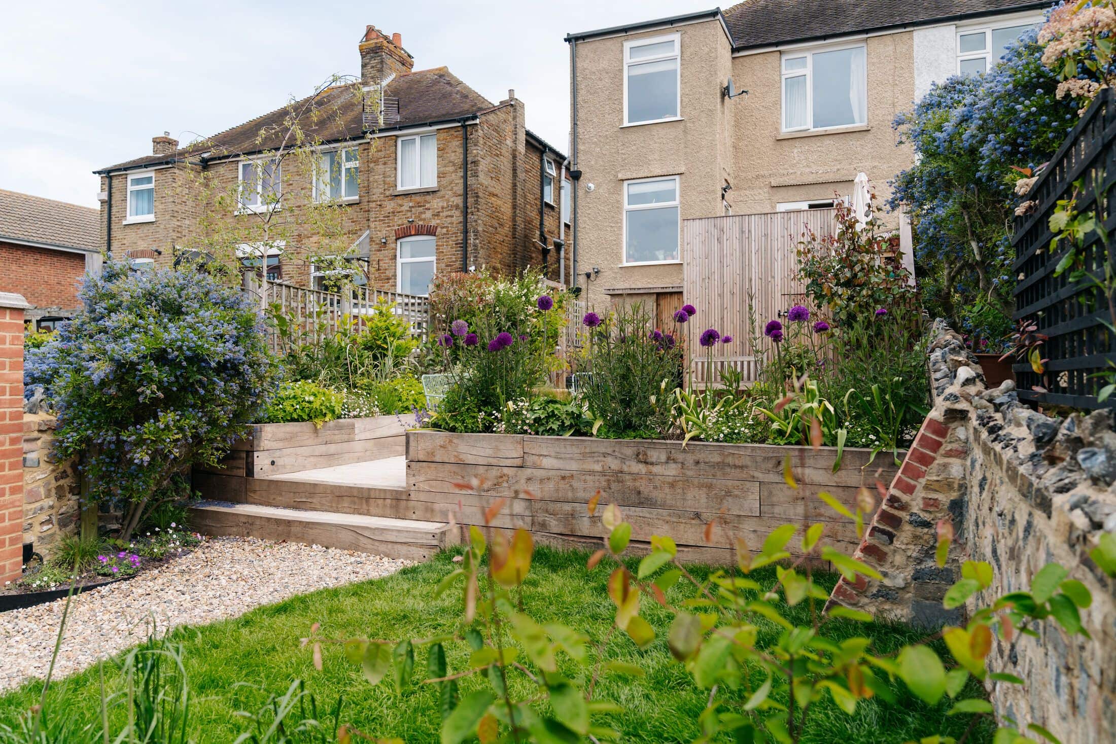 Landscaped town garden with sleeper raised beds, a lawn and a flint and brick boundary wall