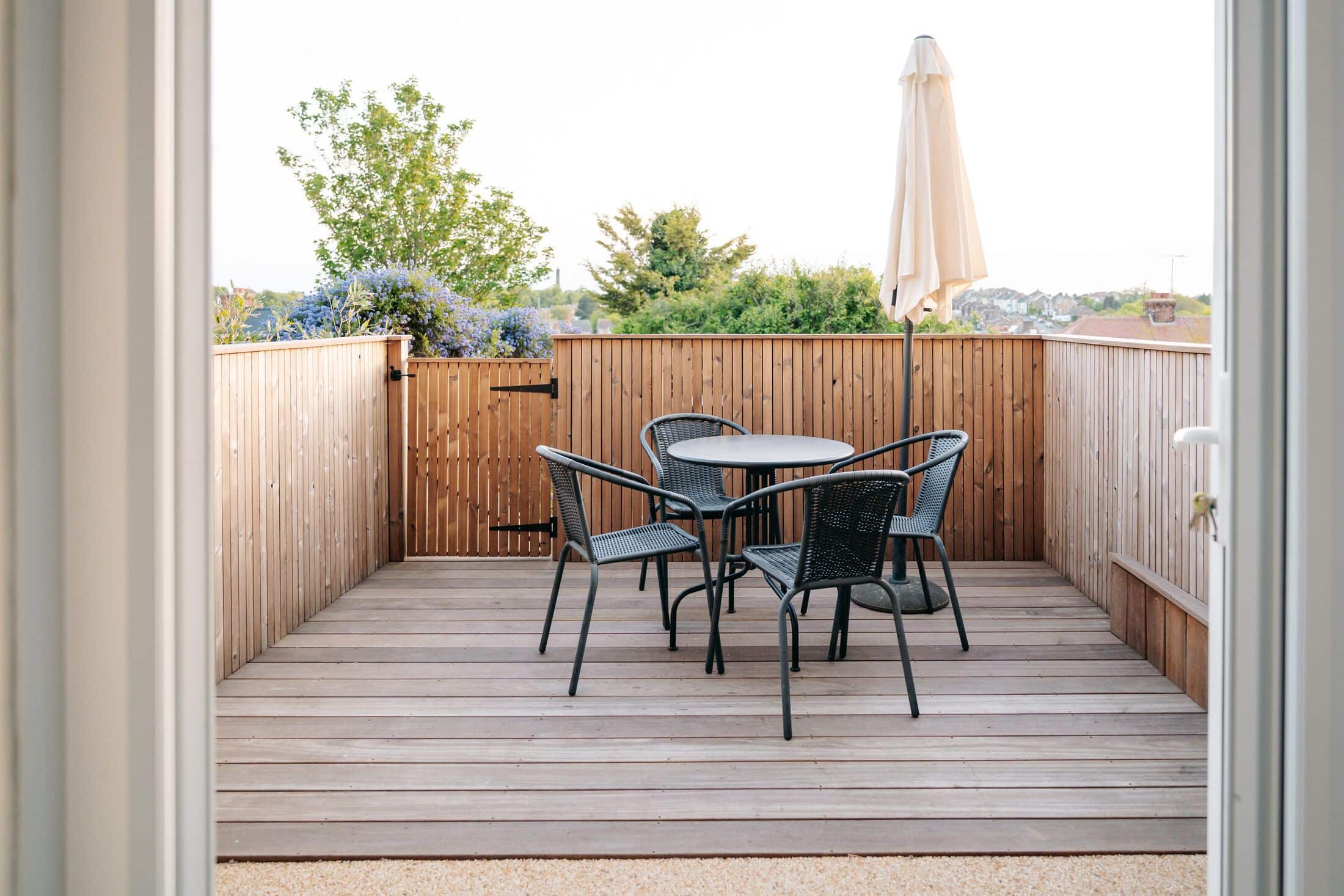 Timber-decked roof terrace with black bistro furniture and a parasol overlooking Thanet rooftops