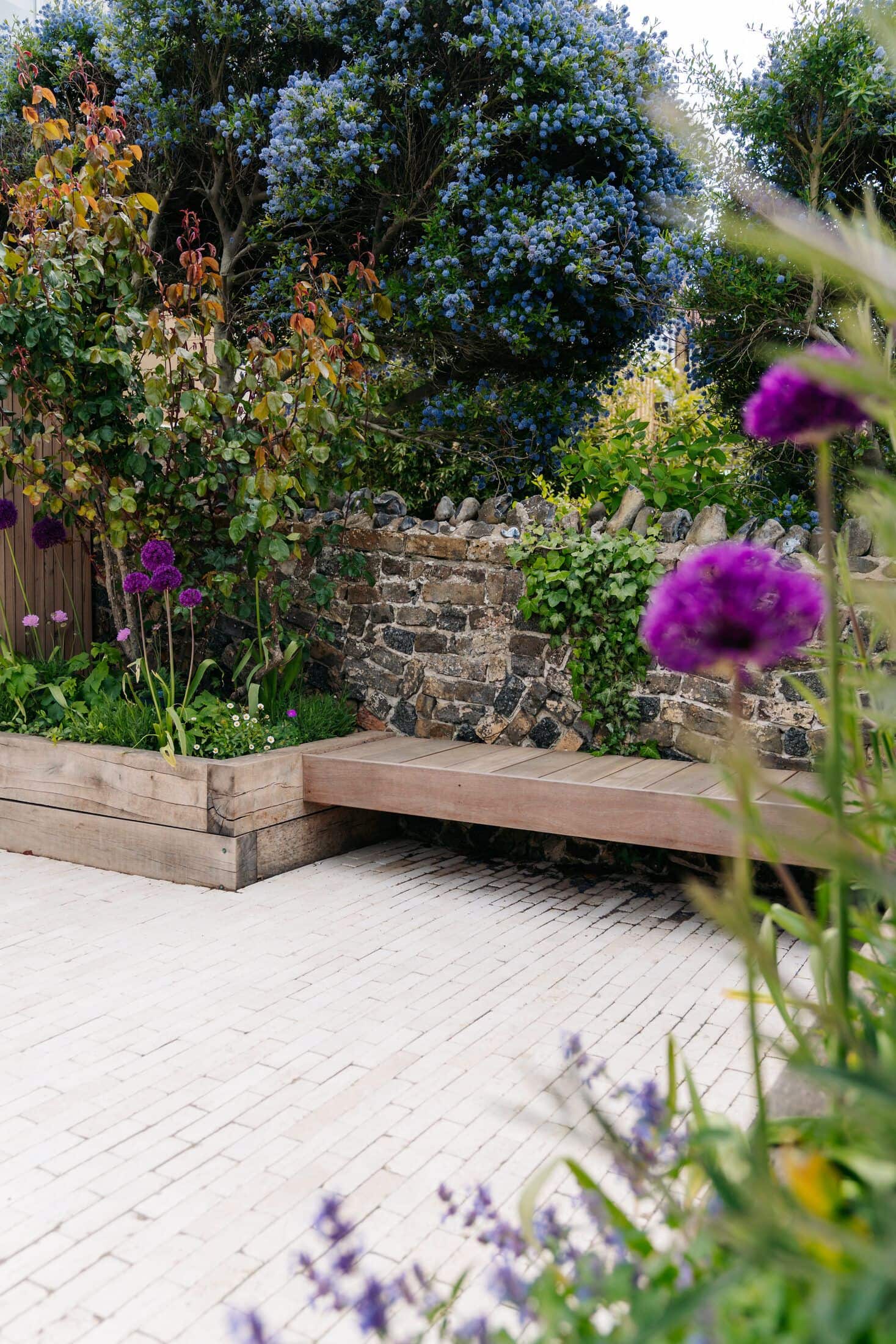 Clay-paver patio with a built-in timber bench against a flint and brick wall