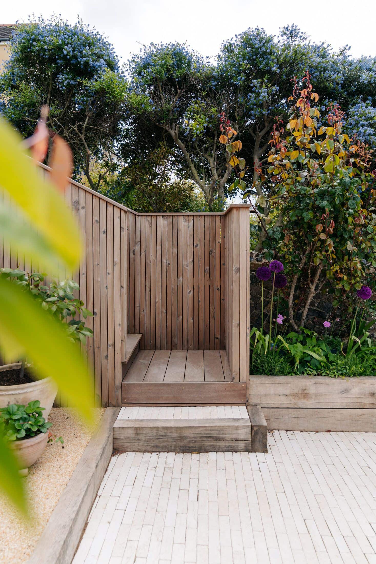 Timber bench and sleeper step on a clay-paver patio against a flint and brick wall