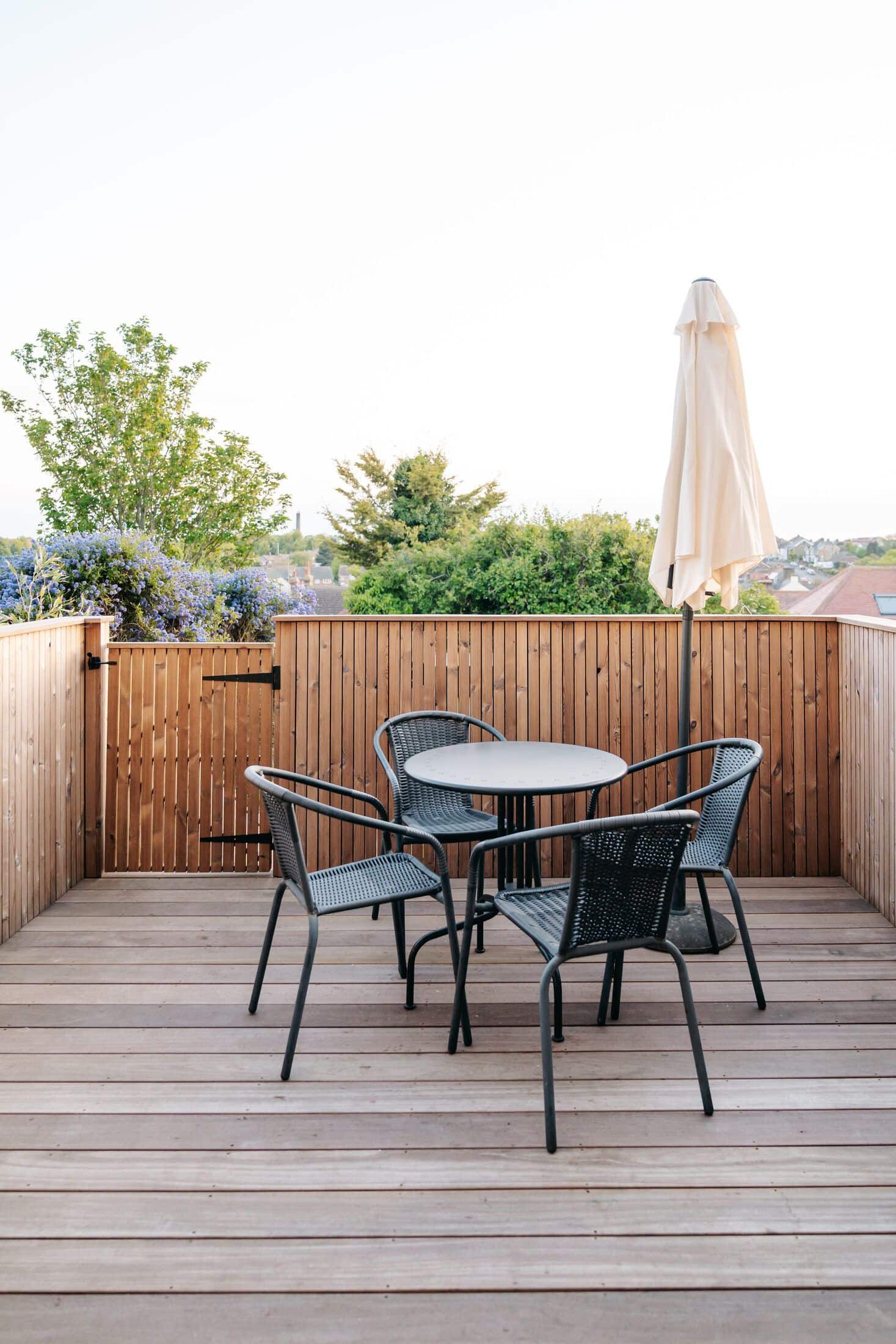 Timber-decked roof terrace with black bistro furniture and a coastal town view