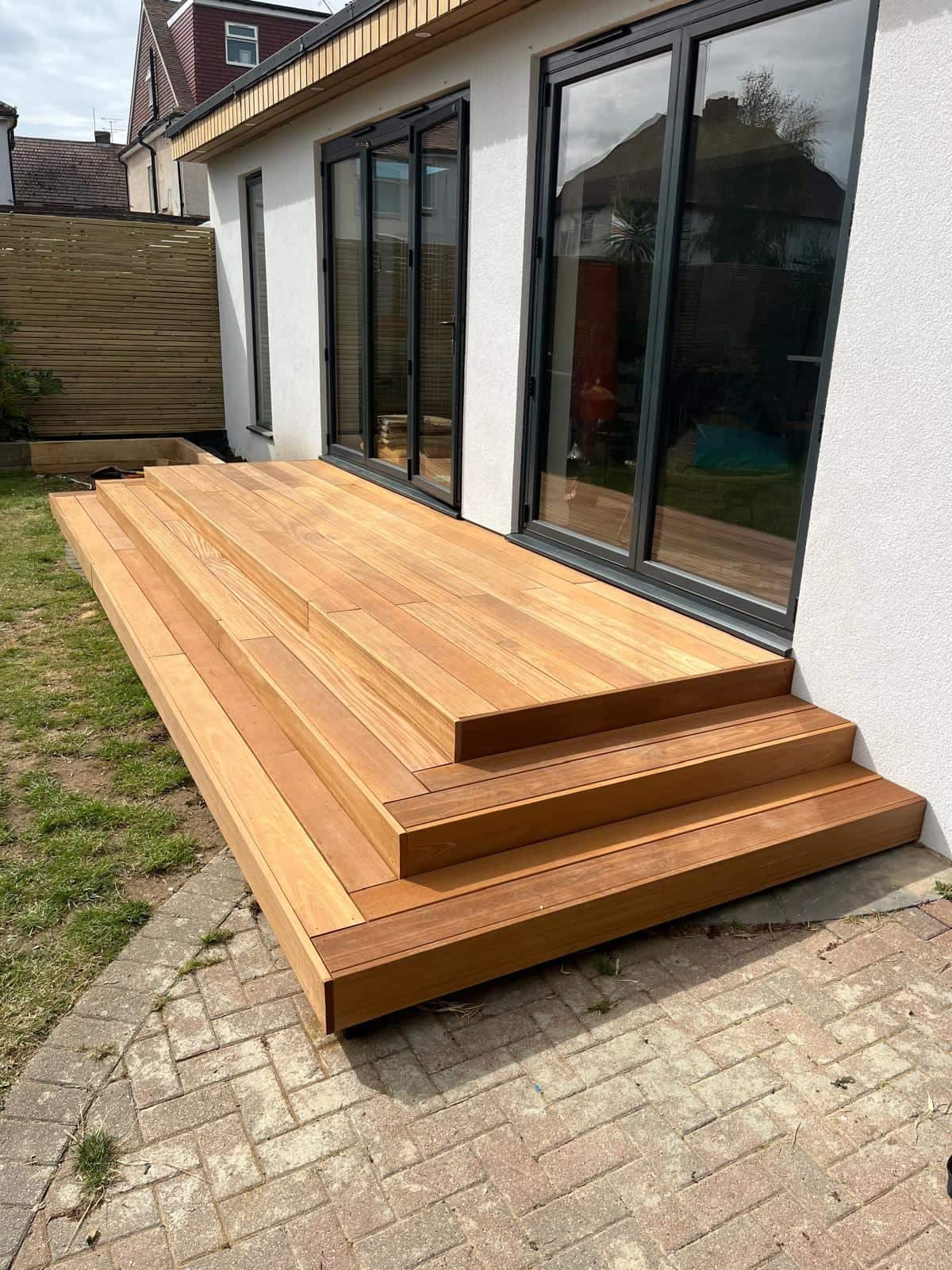 Hardwood deck with three wrap-around steps leading down from grey aluminium bi-fold doors on a rendered extension