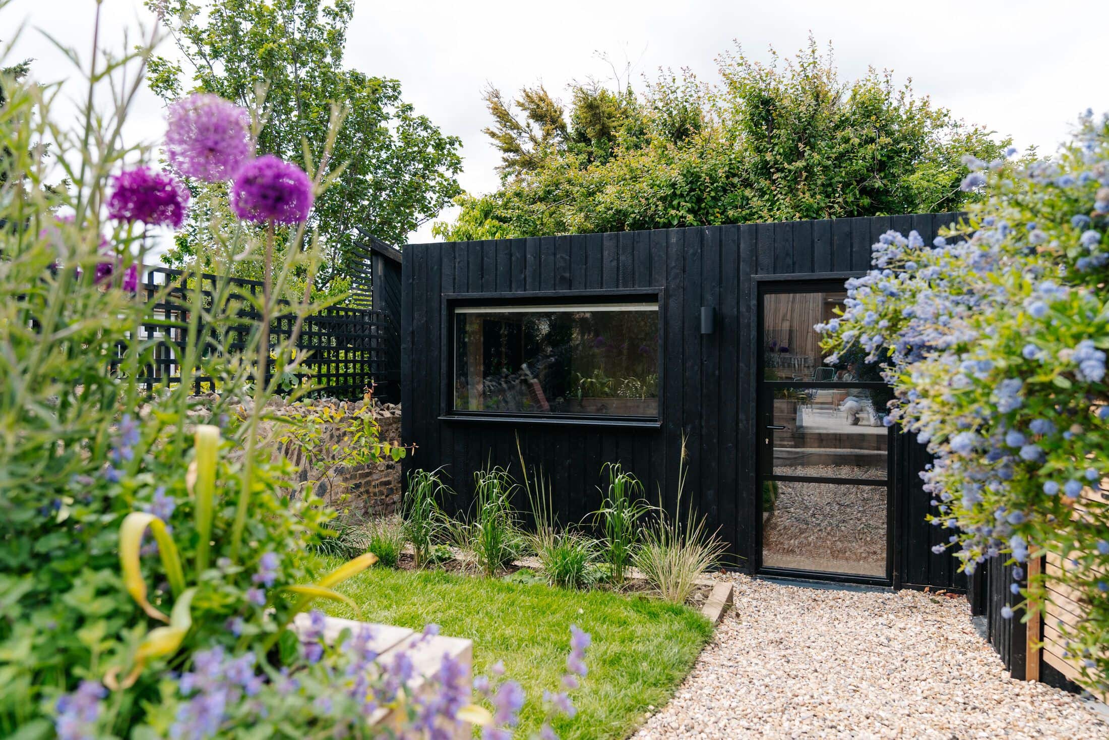 Gravel path leading to the glazed door of a black charred-timber garden studio