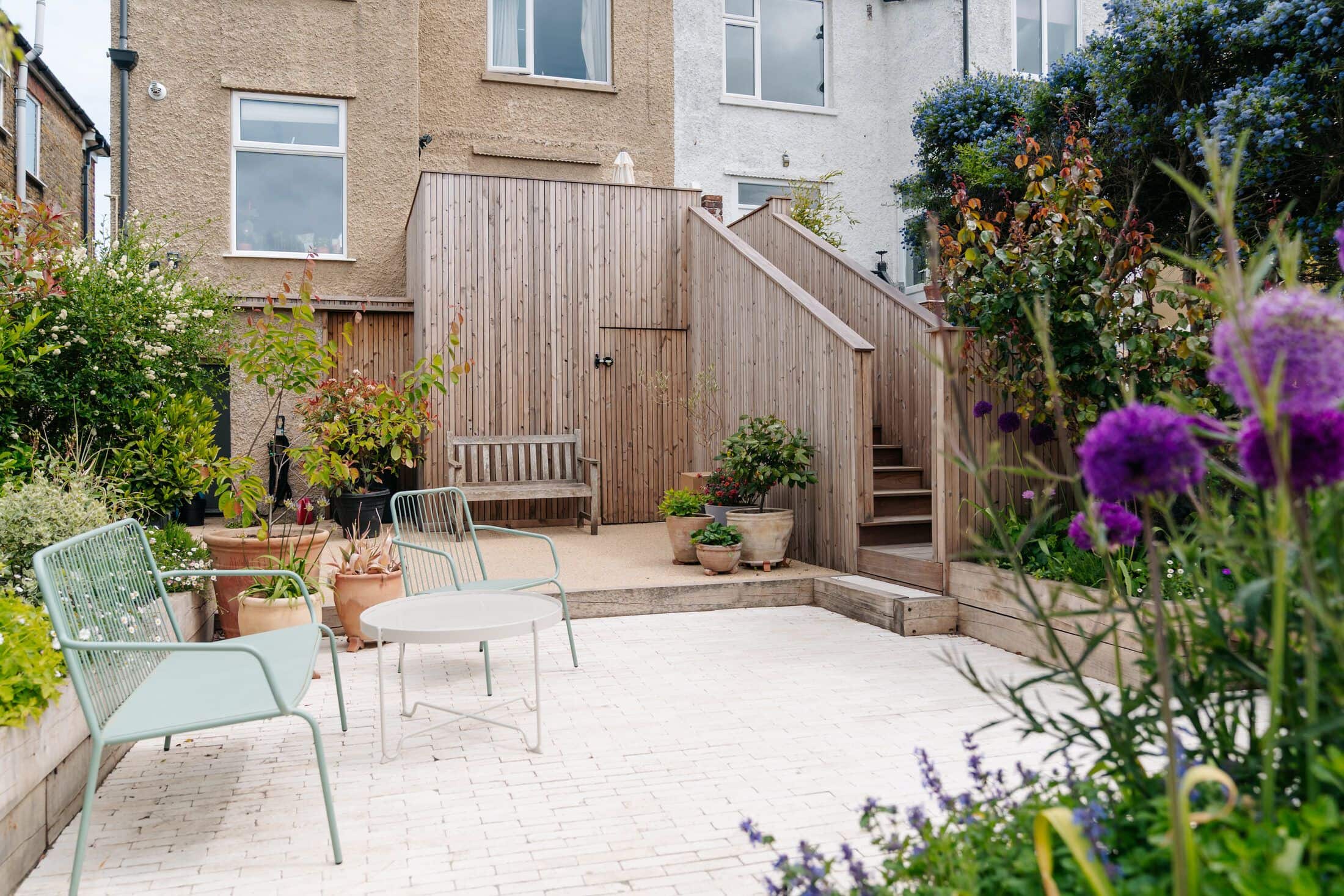 Paved courtyard with sage-green bistro furniture, a timber-clad garden store and steps up to a period house