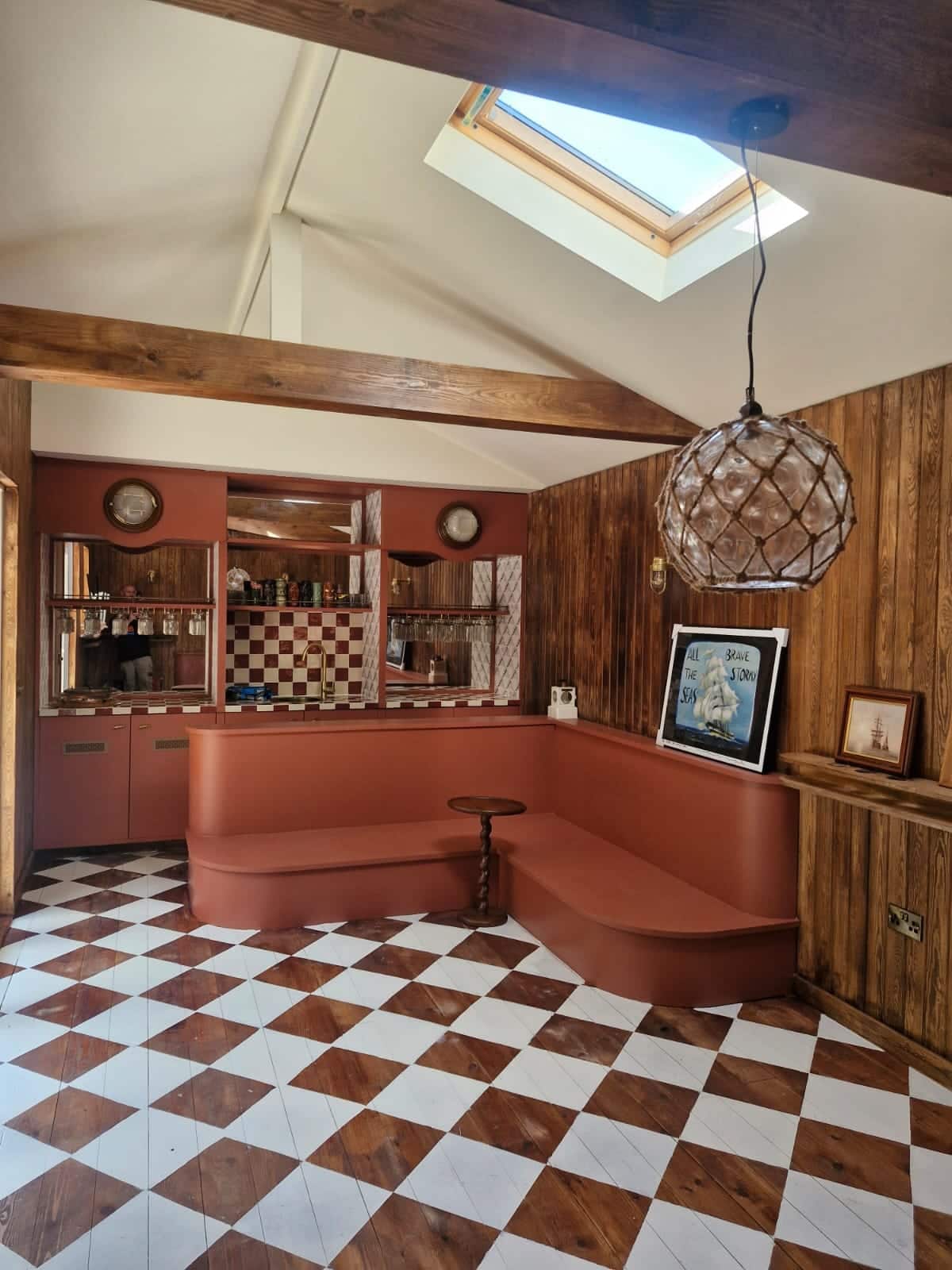 Bespoke terracotta-painted home bar and curved built-in seating in a timber-panelled snug with a chequerboard painted floor