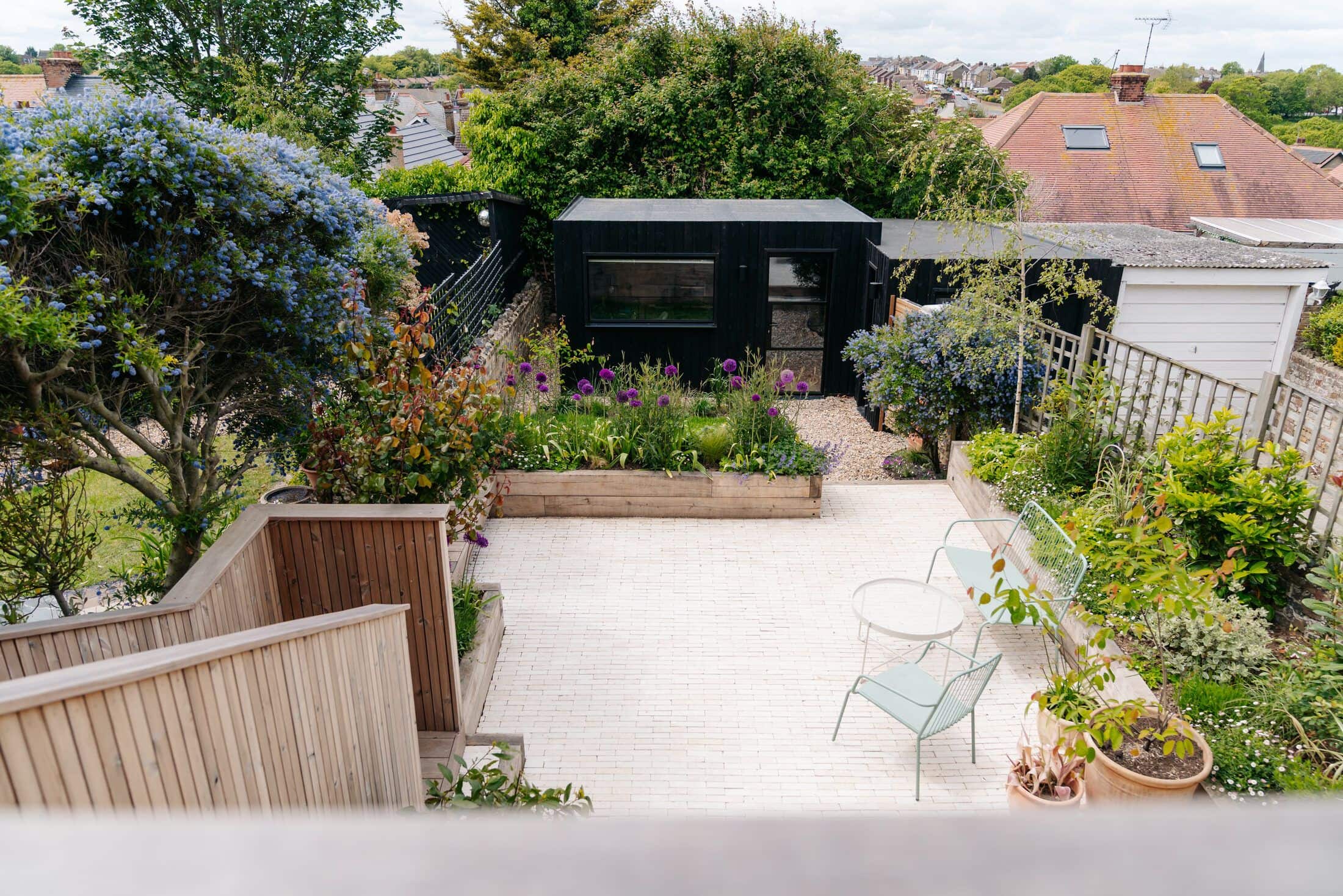 Elevated view of a landscaped town garden with a black-clad garden studio, paved patio and flowering borders