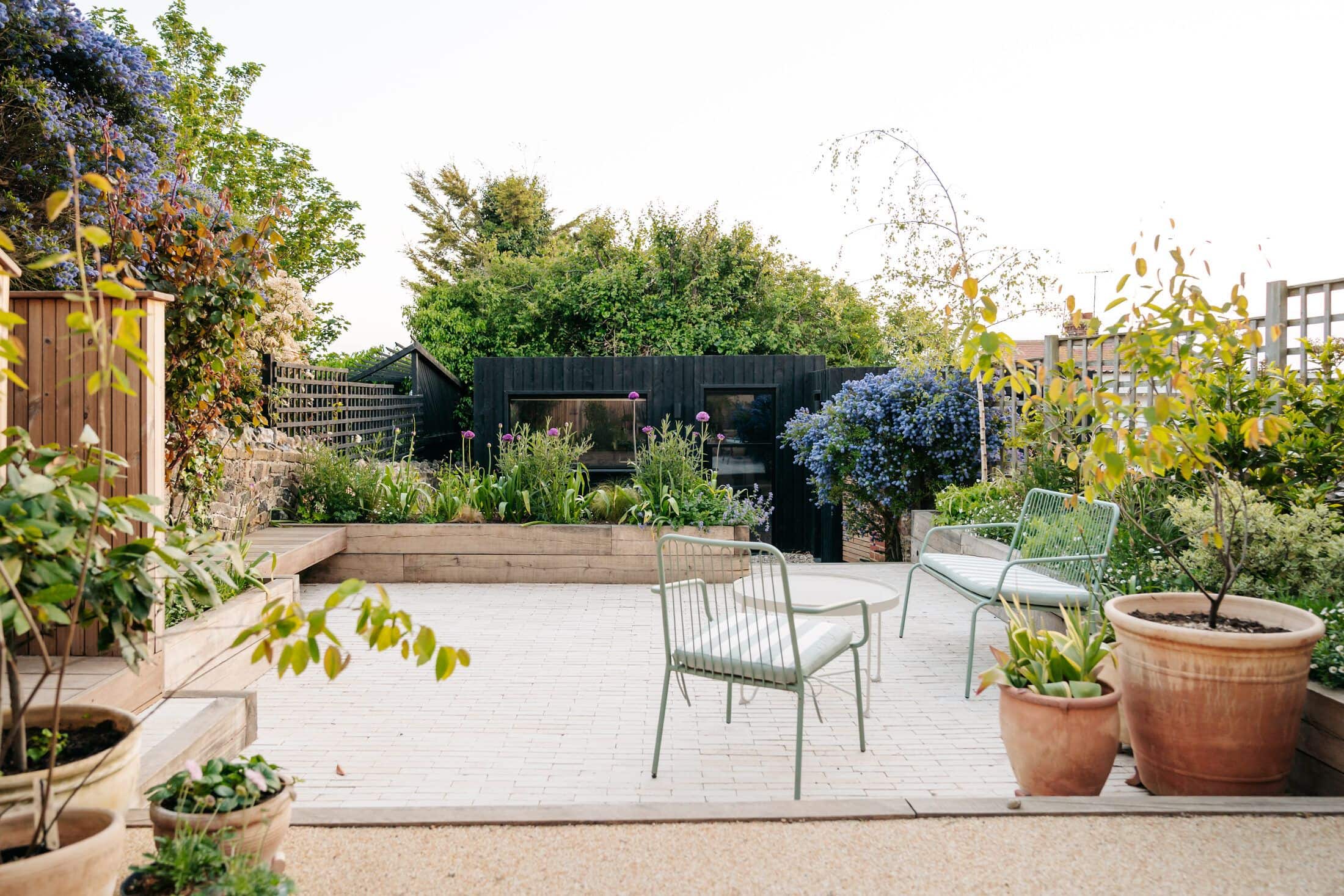 Landscaped courtyard with resin-bound gravel, sleeper raised beds in full flower and sage-green metal chairs