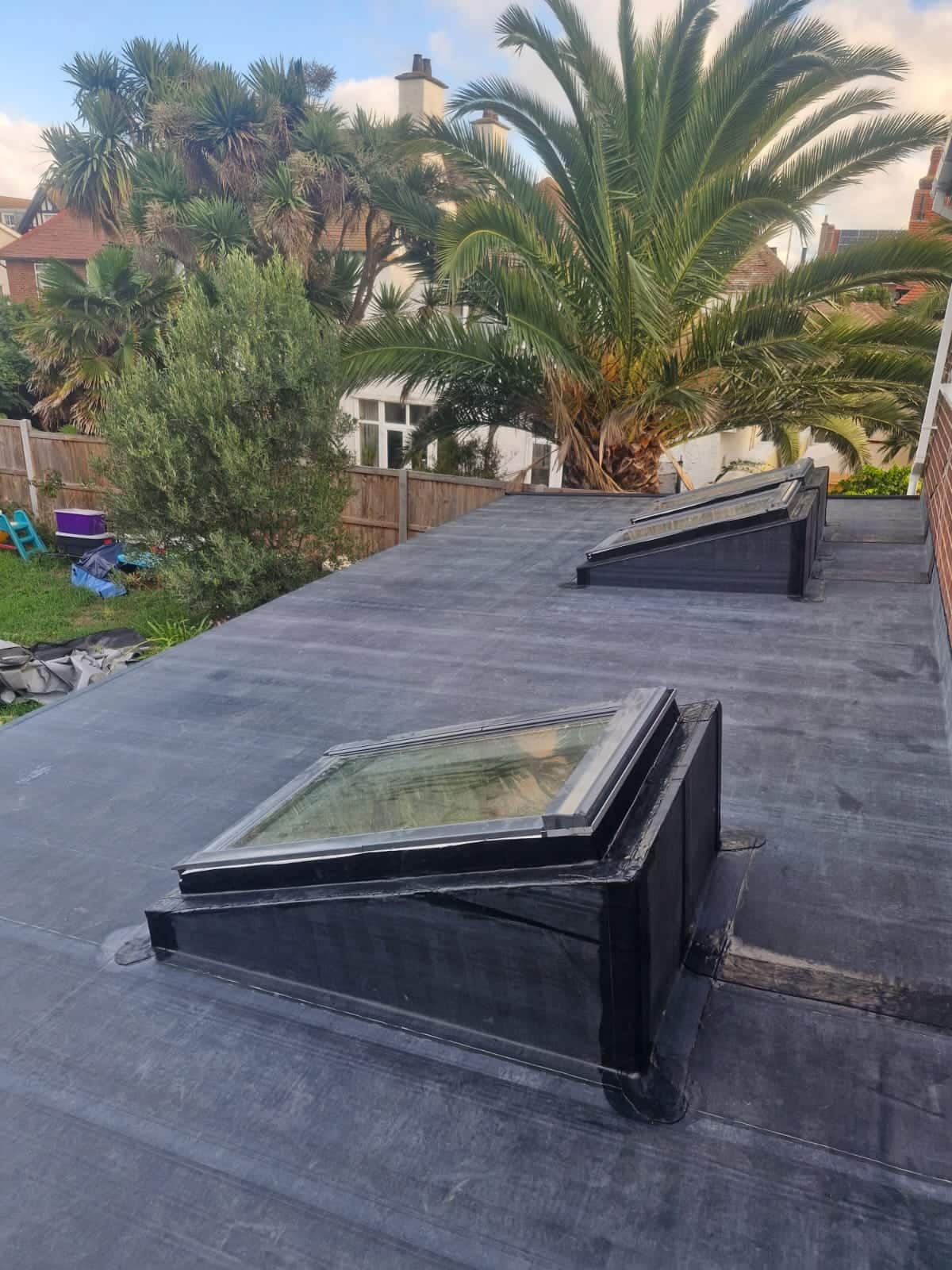 Finished flat roof on a rear extension with two Velux roof lights, palm trees and a coastal house beyond